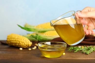 Photo of Woman pouring fresh corn oil into bowl on wooden table