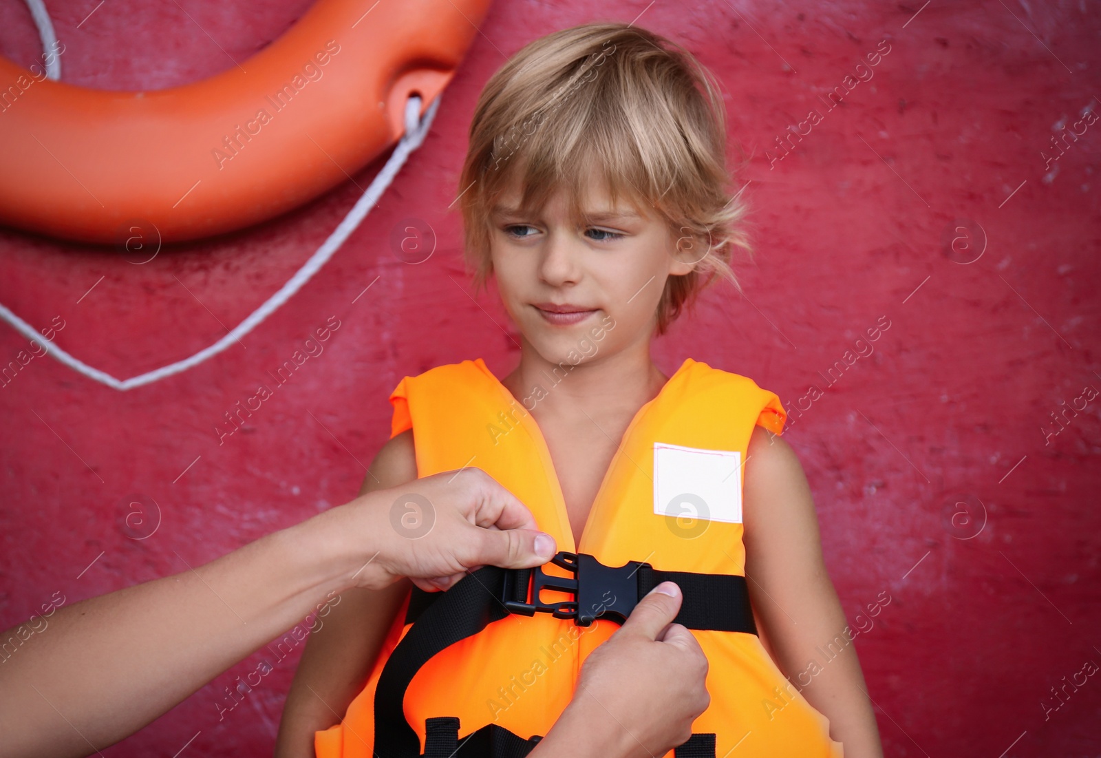 Photo of Rescuer putting orange life vest on child near red wall