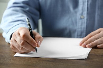 Photo of Man writing on sheet of paper with pen at wooden table, closeup