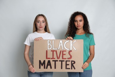 Photo of Women holding sign with phrase Black Lives Matter on grey background. Racism concept