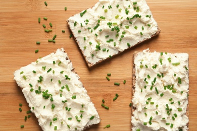 Tasty snack with cream cheese on wooden table, flat lay