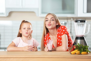 Young woman and her daughter with glasses of delicious milk shakes in kitchen