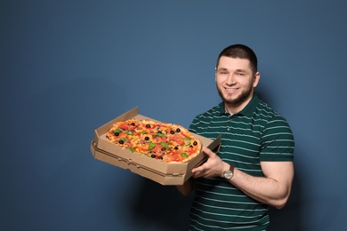 Attractive young man with delicious pizza on color background