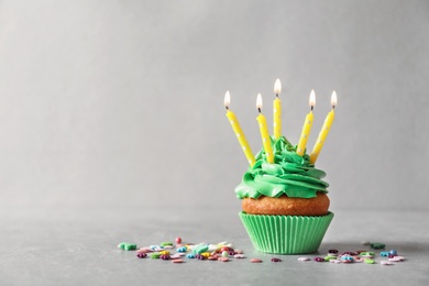 Photo of Delicious birthday cupcake with candles on grey background