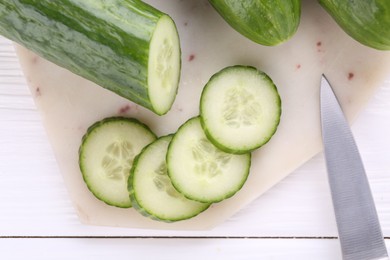 Photo of Cucumbers, knife and marble cutting board on white wooden table, top view