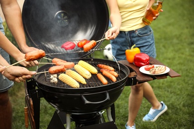 Photo of People with sausages near barbecue grill outdoors, closeup