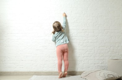 Little girl drawing on white brick wall, back view. Child`s art