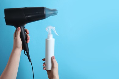 Photo of Woman holding spray bottle with thermal protection and hairdryer on light blue background, closeup. Space for text