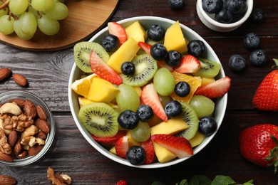 Photo of Tasty fruit salad in bowl and ingredients on wooden table, flat lay