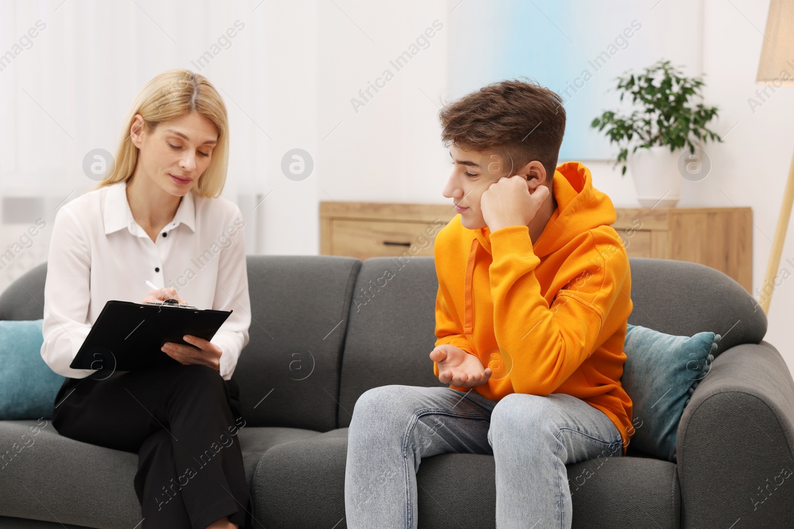 Photo of Psychologist working with teenage boy on sofa in office