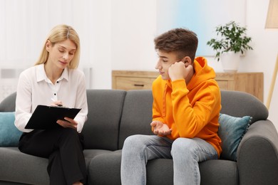 Photo of Psychologist working with teenage boy on sofa in office