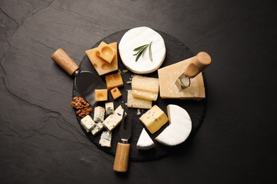 Photo of Cheese platter with specialized knives and fork on black table, flat lay