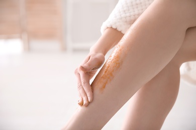 Woman applying body scrub on legs, closeup