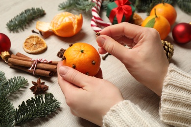 Photo of Woman decorating tangerine with cloves at light wooden table, closeup. Christmas atmosphere