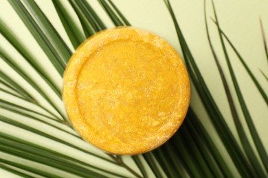 Photo of Orange solid shampoo bar and leaf on green background, top view. Hair care
