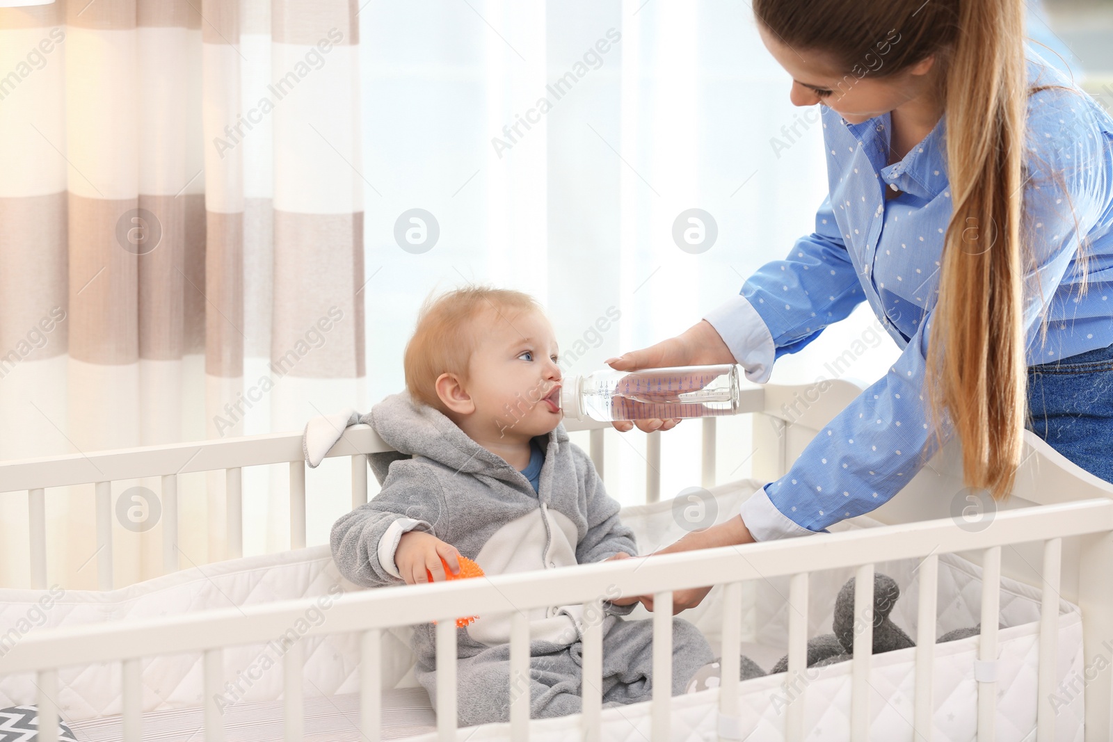 Photo of Teen nanny giving cute little baby water from bottle at home