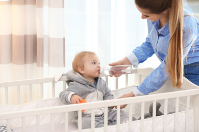 Teen nanny giving cute little baby water from bottle at home