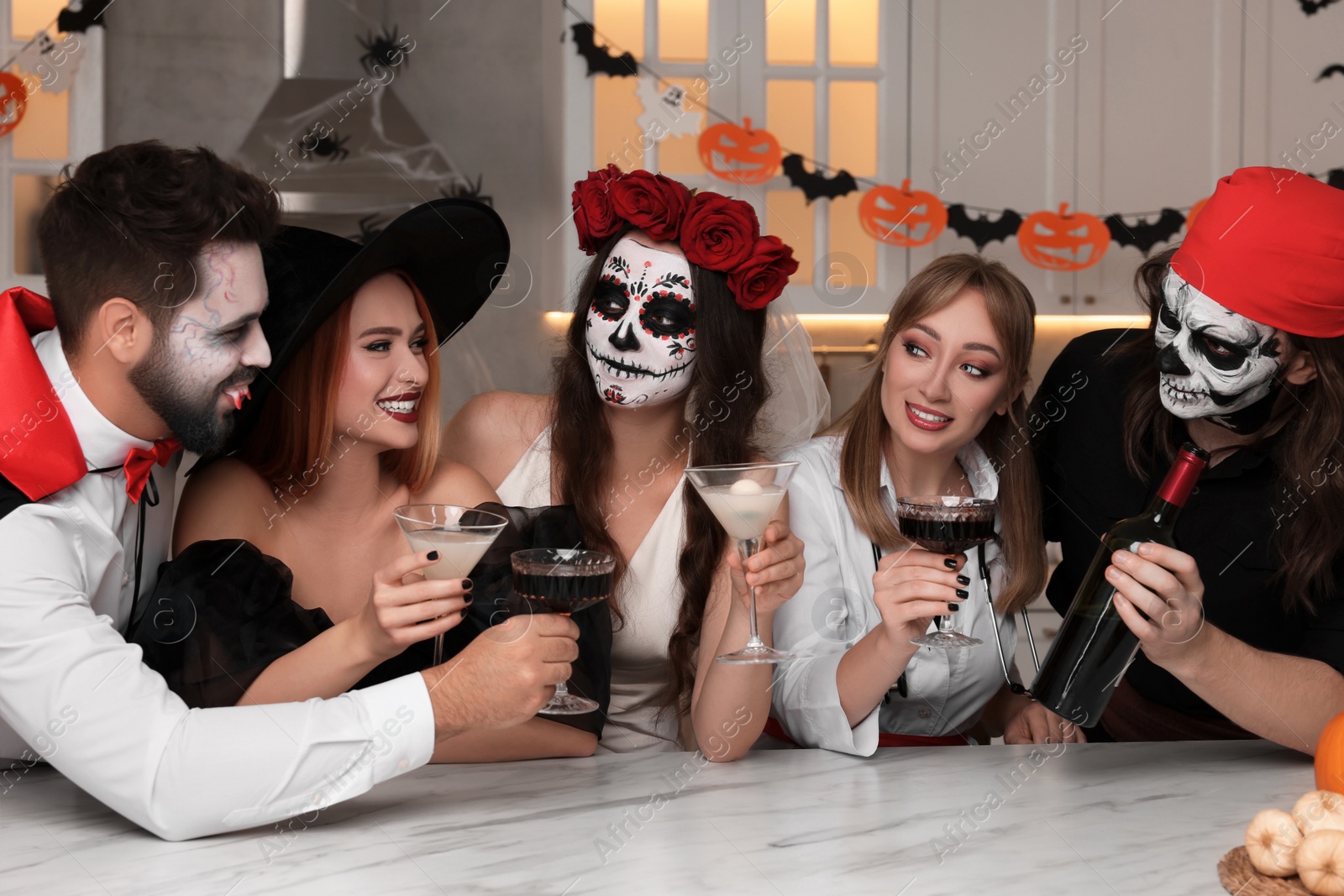 Photo of Group of people in scary costumes with cocktails celebrating Halloween indoors