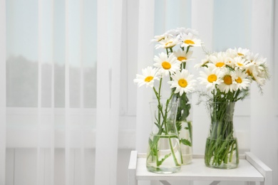 Photo of Vases with beautiful chamomile flowers on table