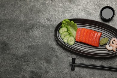 Photo of Tasty salmon slices, shrimp, cucumber and lettuce on grey table, flat lay with space for text. Delicious sashimi dish