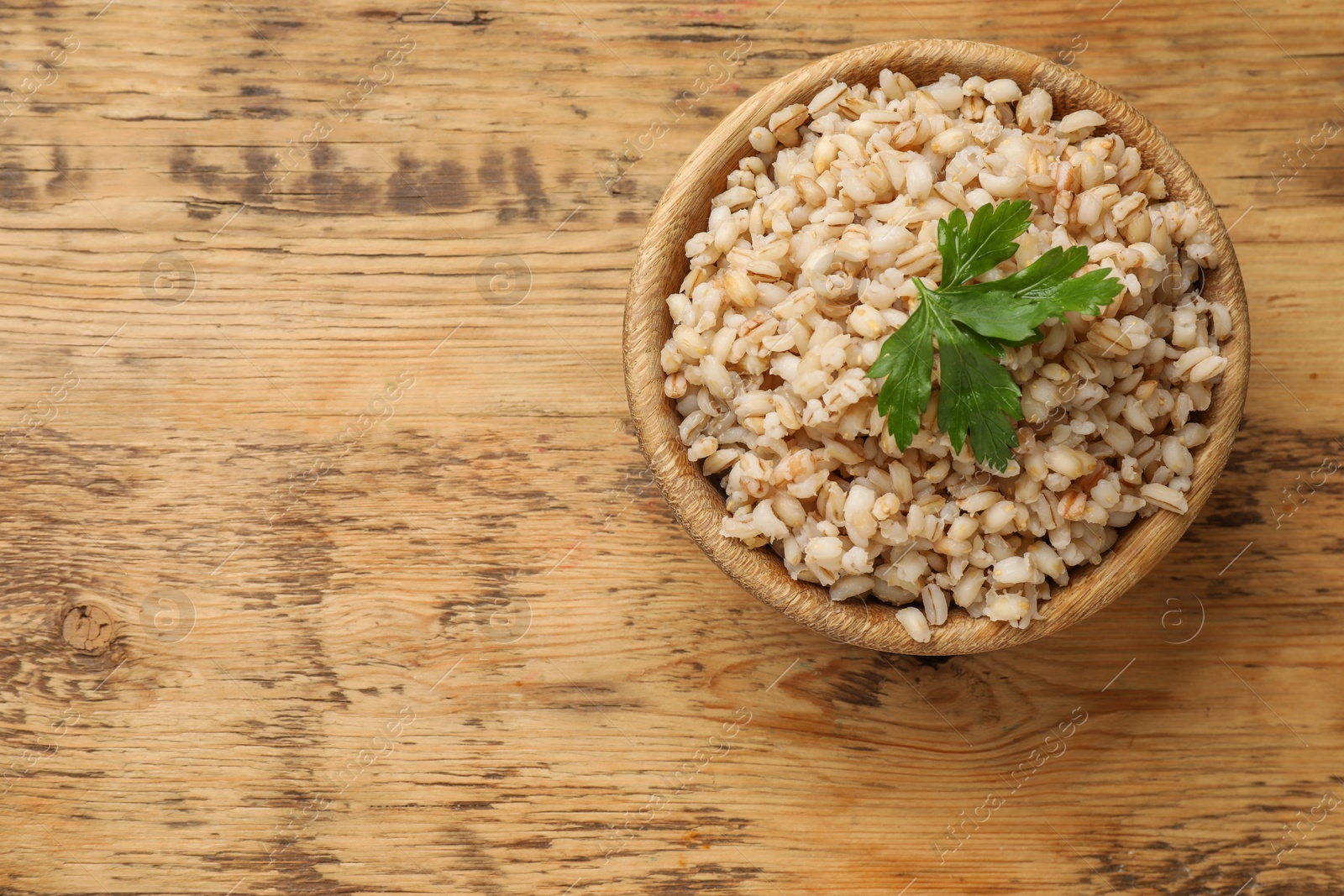 Photo of Delicious pearl barley with parsley in bowl on wooden table, top view. Space for text