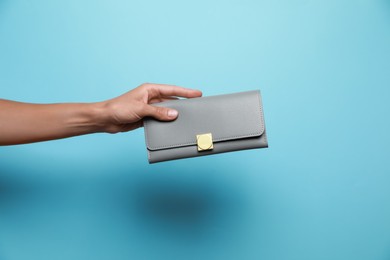 Photo of Woman holding leather purse on light blue background, closeup