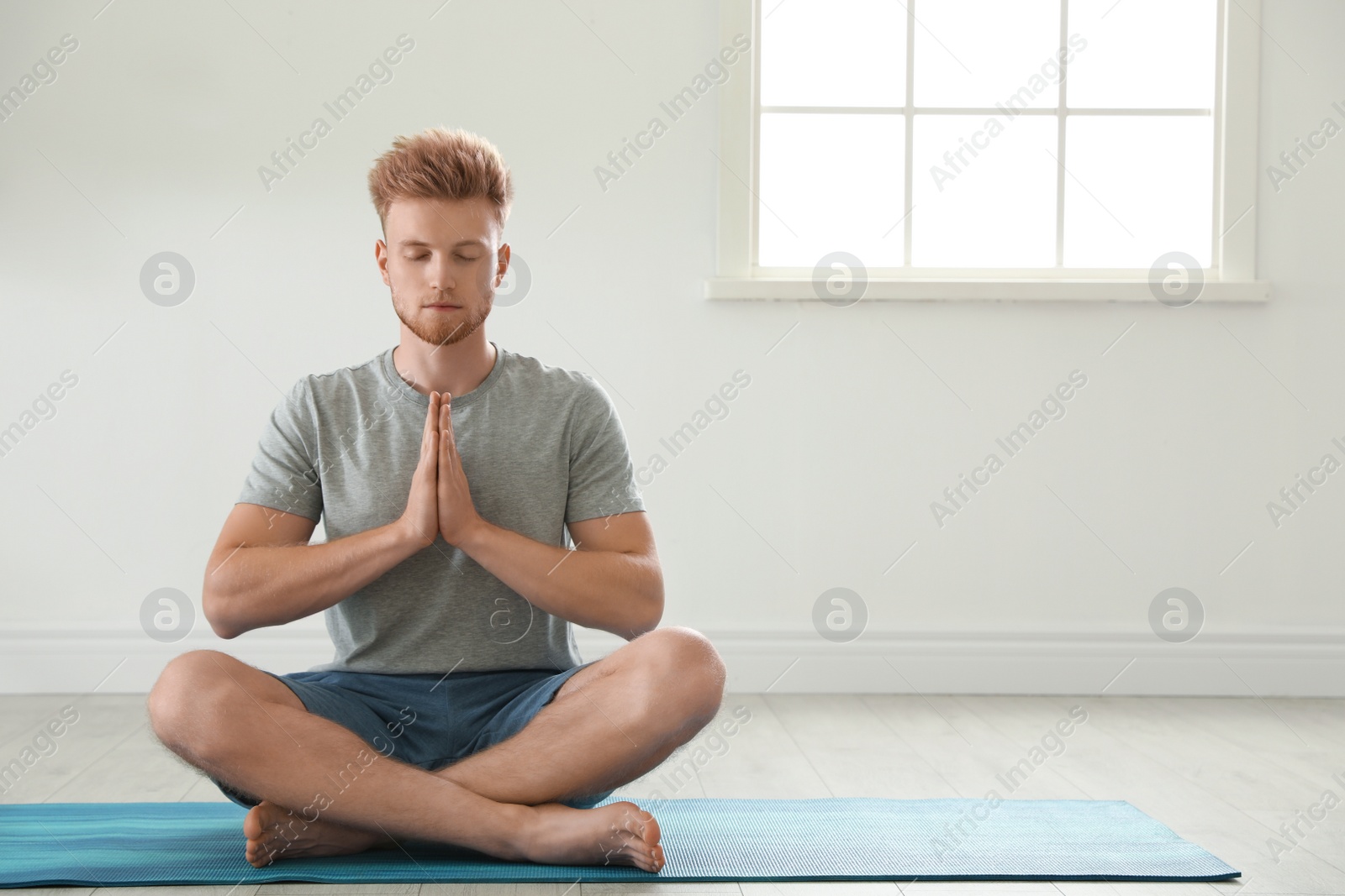 Photo of Handsome young man practicing zen yoga indoors, space for text