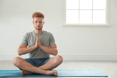 Photo of Handsome young man practicing zen yoga indoors, space for text