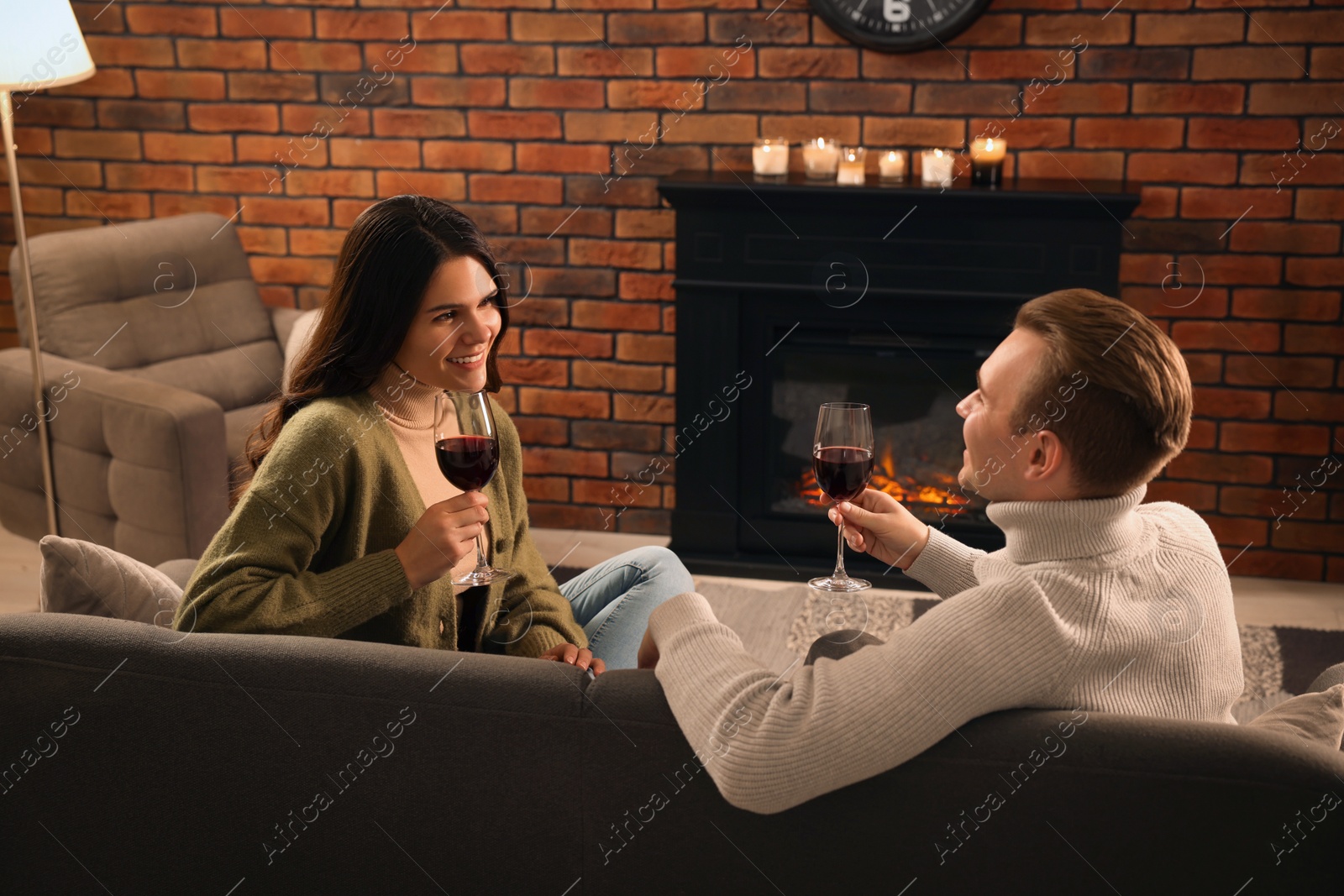 Photo of Happy lovely couple with glasses of wine spending time together near fireplace at home