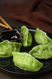 Photo of Delicious green dumplings (gyozas) and soy sauce on wooden table, closeup