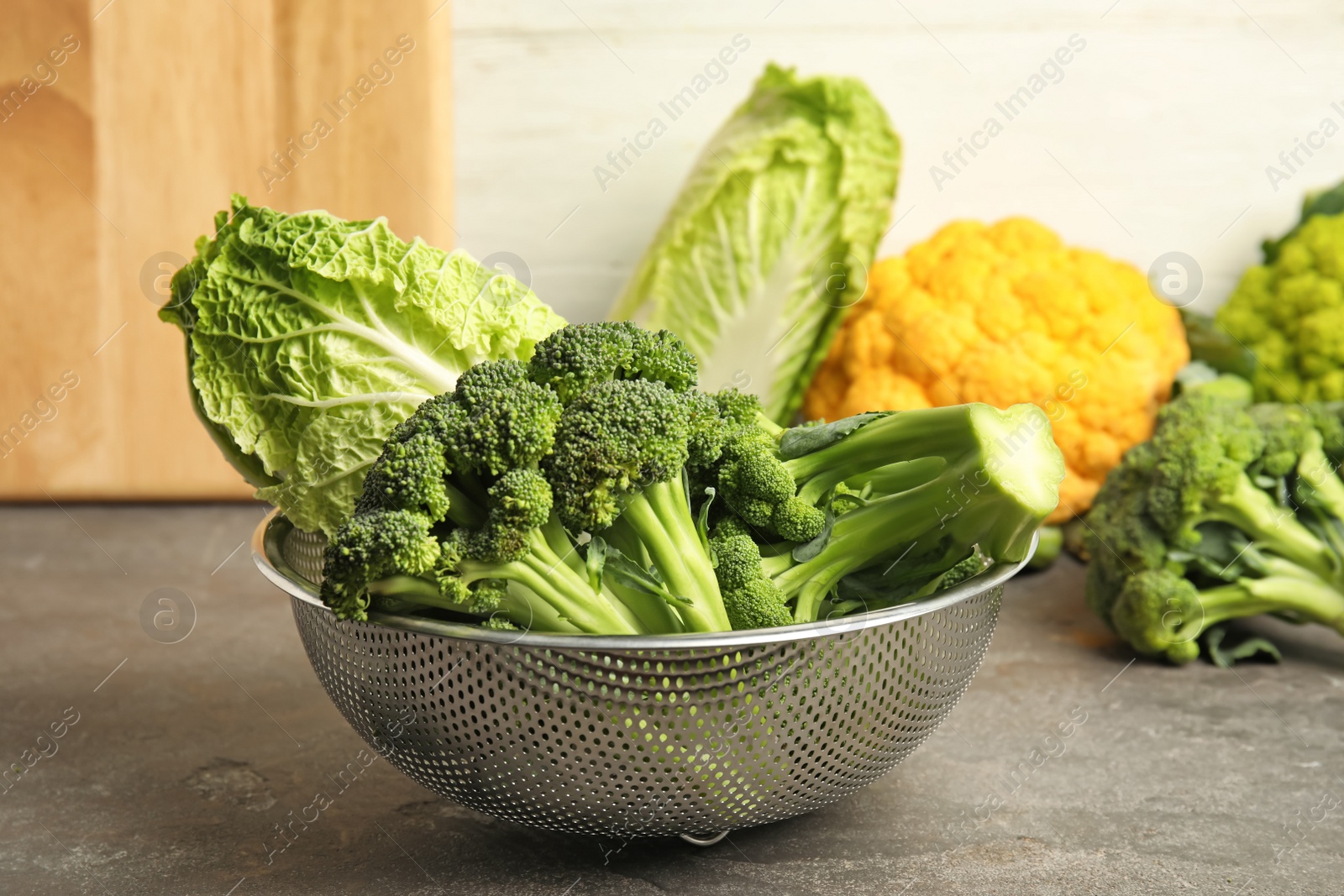 Photo of Colander with different fresh cabbages on table. Healthy food