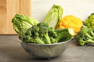 Photo of Colander with different fresh cabbages on table. Healthy food