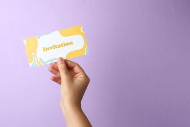 Woman holding beautiful card with word Invitation on lilac background, closeup. Space for text