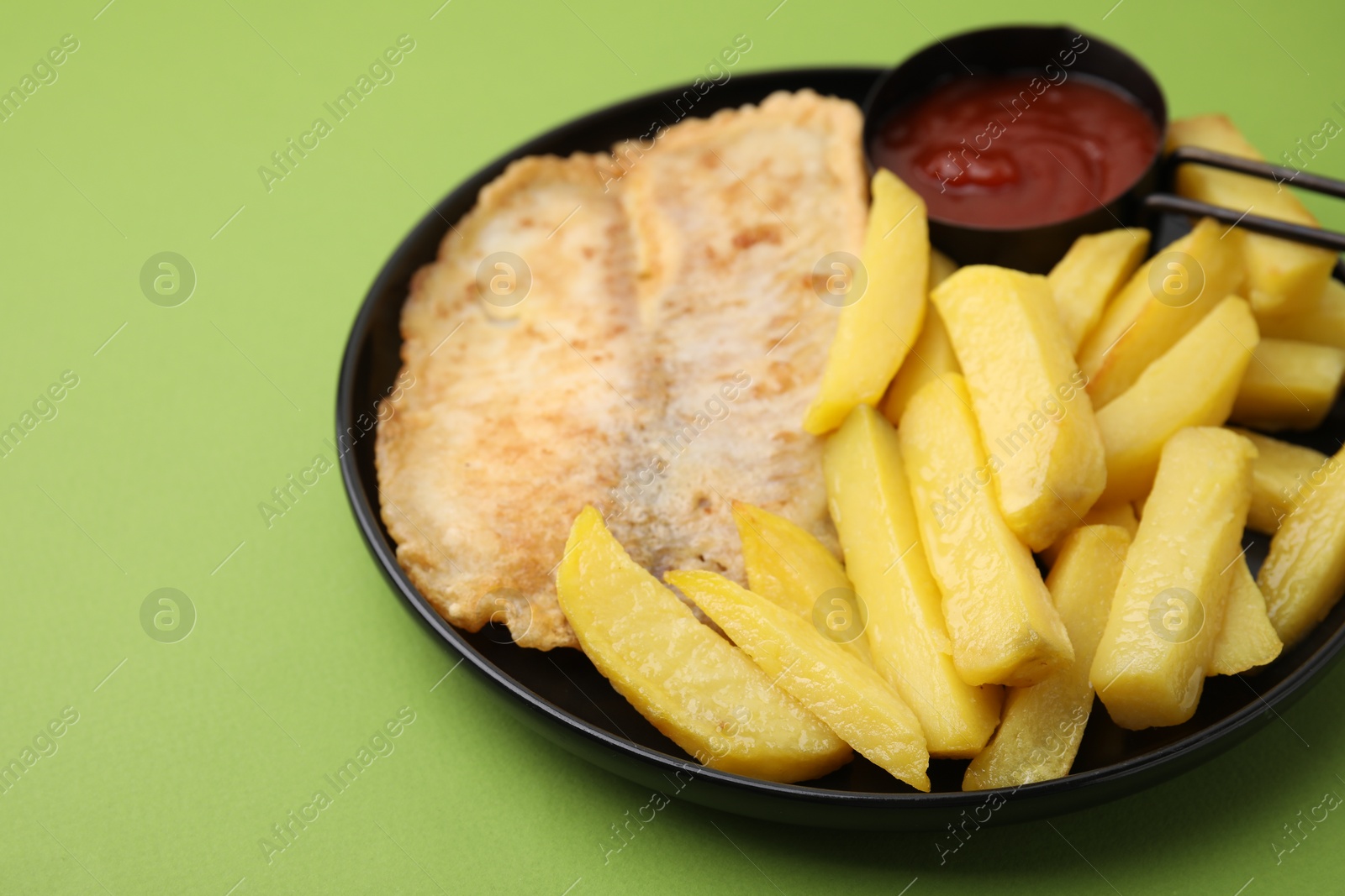 Photo of Delicious fish and chips with ketchup on green table, closeup