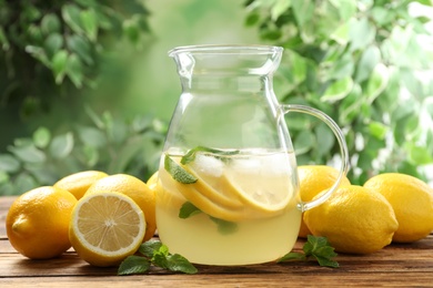 Photo of Natural lemonade with mint and fresh fruits on wooden table against blurred background. Summer refreshing drink