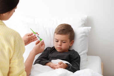 Mother measuring temperature of her sick son in bed