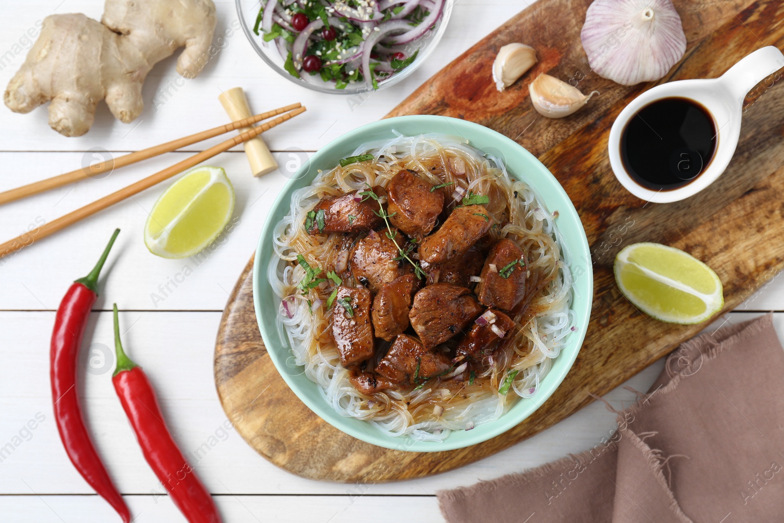 Photo of Bowl with pieces of soy sauce chicken and noodle on white wooden table, flat lay