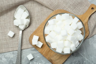 Photo of White sugar cubes in glass bowl on grey table, flat lay