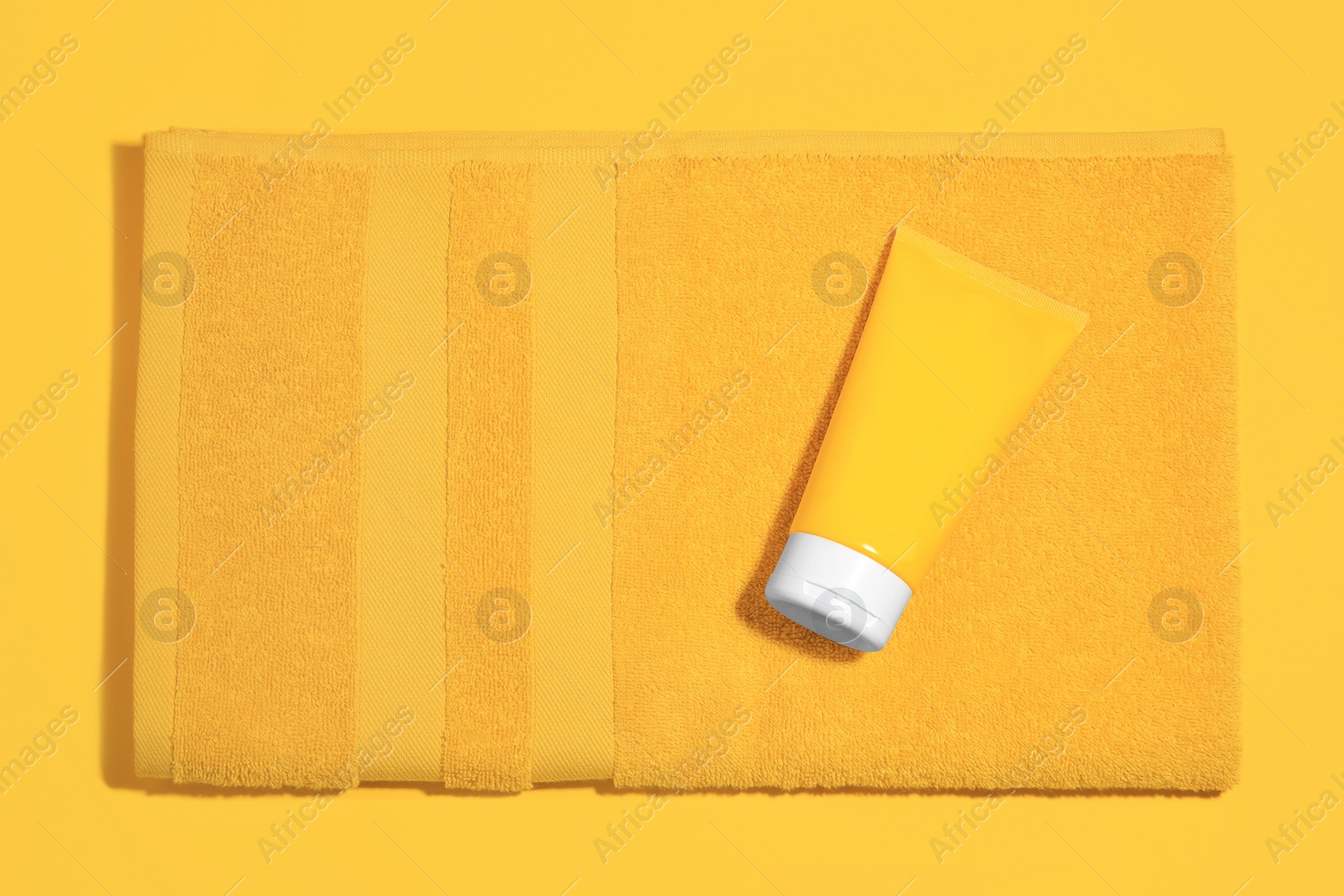 Photo of Sunscreen and towel on orange background, top view. Sun protection