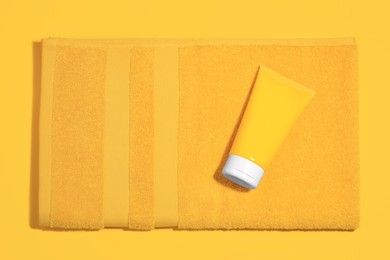 Photo of Sunscreen and towel on orange background, top view. Sun protection
