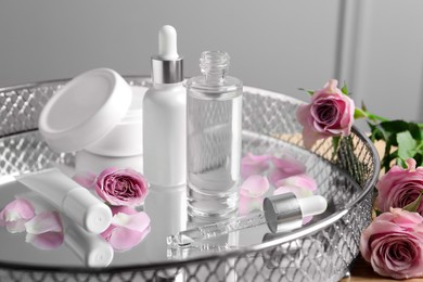 Bottles of cosmetic serum, beauty products and flowers on table