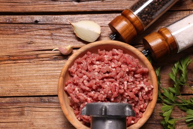 Manual meat grinder with beef mince, onion, garlic, parsley and spices on wooden table, flat lay