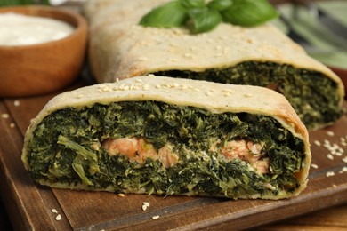 Photo of Piece of tasty strudel with salmon and spinach on wooden board, closeup