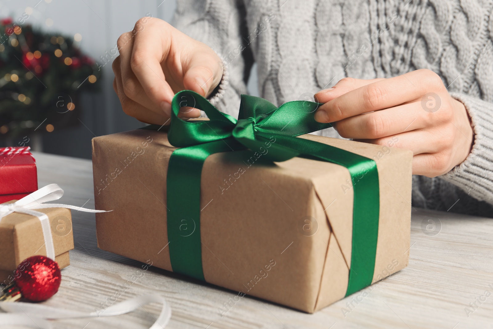 Photo of Woman decorating gift box at white wooden table, closeup. Christmas present