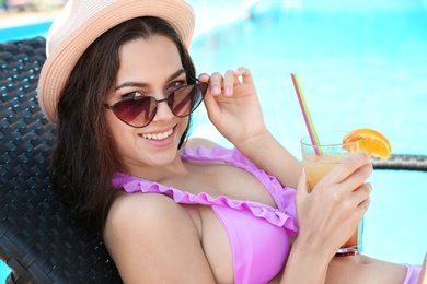 Photo of Beautiful young woman with cocktail wearing bikini on sunbed near swimming pool
