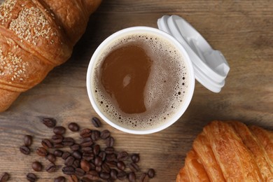 Photo of Coffee to go. Paper cup with tasty drink, croissants and beans on wooden table, flat lay