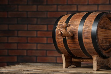 Wooden barrel with tap on table near brick wall, space for text