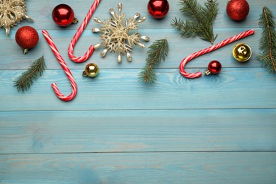 Flat lay composition with tasty candy canes and Christmas decor on light blue wooden table, space for text