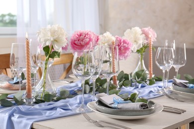 Photo of Beautiful table setting. Plate with greeting card, napkin and branch near glasses, peonies, burning candles and cutlery on table indoors