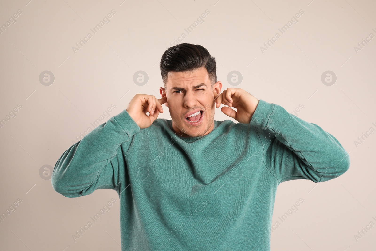 Photo of Emotional man covering ears with fingers on beige background